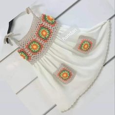 a white dress with orange and green flowers on it's chest, hanging from a hook