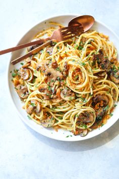 a white bowl filled with pasta and mushrooms on top of a table next to a wooden spoon