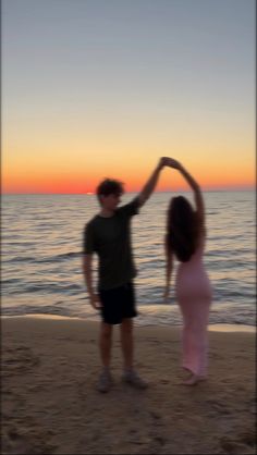 two people standing on the beach with their arms in the air and one person holding his hand up