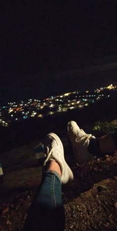 a person's feet with their shoes up on the ground at night overlooking a city