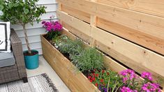 a wooden planter filled with lots of flowers next to a bench on the side of a house