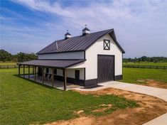 a large white barn with a black roof and two stalls on the side of it