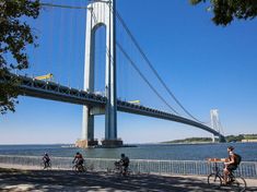 people riding bikes near the water under a bridge