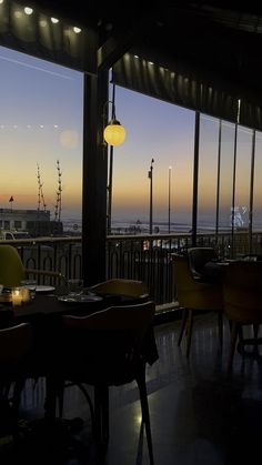 a restaurant with large windows overlooking the ocean at sunset or dawn, and lit candles on tables in front of them