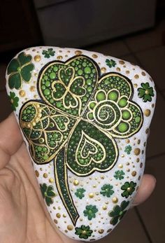 a hand holding a white and green rock with four leaf clovers painted on it