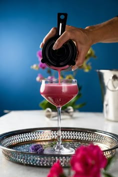 a person pours a drink into a glass on a tray with flowers in the background