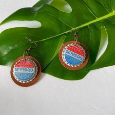 two bottle caps are hanging from a green leaf with the words diet pepsi cola on them