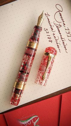 a red and gold fountain pen sitting on top of a notepad next to an envelope