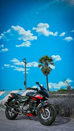 a red and black motorcycle parked on the side of a road next to a palm tree