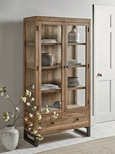 a wooden cabinet with glass doors and drawers in the corner next to a potted plant