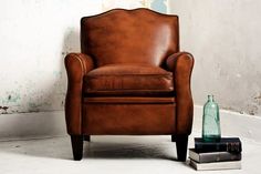 a brown leather chair sitting next to a book and glass bottle on top of a table