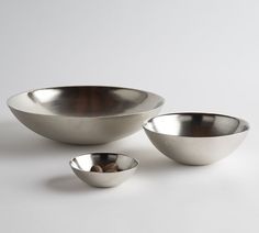 three metal bowls sitting next to each other on a white surface with one bowl in the middle