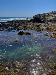 the water is crystal clear and there are rocks on the shore near the ocean with small bubbles in it