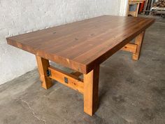 a wooden table sitting on top of a cement floor next to a white brick wall