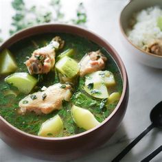 a bowl of soup with meat, cucumbers and rice on the table next to it