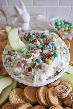 a bowl filled with white chocolate and candy chips next to crackers, apples, and cookies