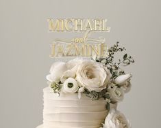 a wedding cake with white flowers on top and gold lettering that reads michael and jazmine