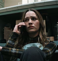 a woman sitting in front of a book shelf talking on a cell phone while holding her hand up to her ear