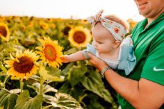 a man holding a baby in front of a field of sunflowers