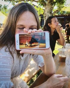 a woman holding up her cell phone to take a selfie at an outdoor table