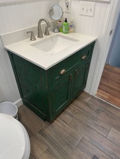 a white sink sitting under a bathroom mirror next to a green cabinet in a bathroom