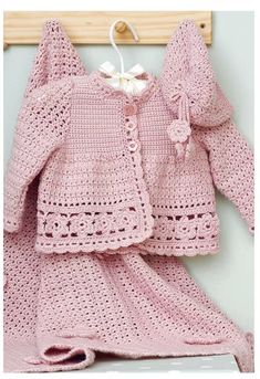 a pink crochet baby dress and coat on a wooden hanger next to a white wall