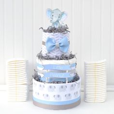 a three tiered baby shower cake with an elephant on top and blue ribbon around the edges