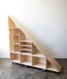 a book shelf under a slanted wall with shelves on wheels and an opening to the bottom