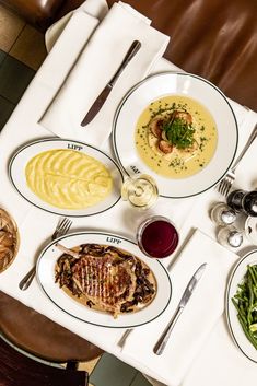 a table topped with plates of food next to wine glasses and utensils on top of a white table cloth