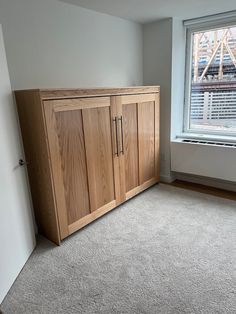 an empty room with a large wooden cabinet next to a window and carpeted floor