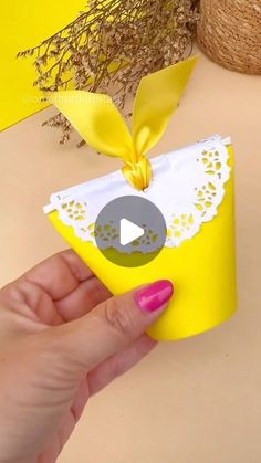 a hand holding a small yellow box with a bow on it's top and a video playing in front of it