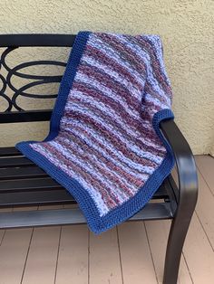 a knitted blanket sitting on top of a wooden bench