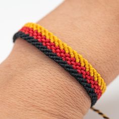 a person wearing a bracelet on their arm with a red, yellow and black stripe