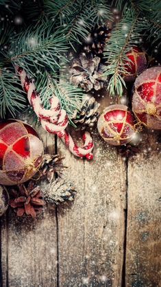 christmas ornaments and pine cones on a wooden surface with snow falling down the top right hand corner