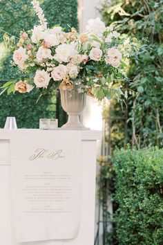 a white sign with flowers on it in front of some bushes