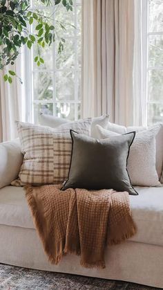 a couch with pillows and blankets on it in front of a window filled with curtains