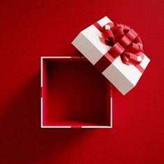 a white gift box with a red bow on the lid and inside it is sitting on a red surface