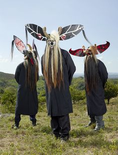 three people with long hair and masks on their heads are standing in the middle of a field