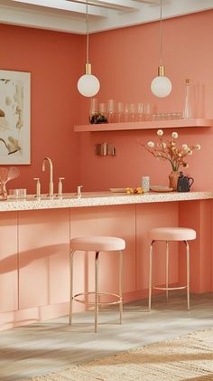 an orange kitchen with pink walls and gold touches on the countertop, along with two stools