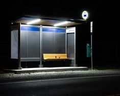 a bus stop sitting on the side of a road at night with a bench in front of it