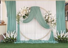 a wedding arch decorated with white flowers and greenery in front of a green drape