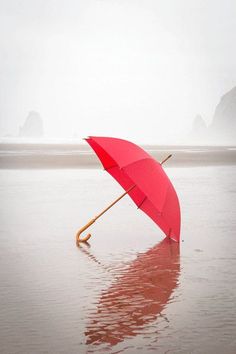 a red umbrella sitting on top of a wet beach next to the ocean with rocks in the background