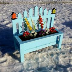 a blue bench with flowers in it sitting in the snow