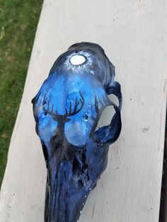 a blue skull with trees painted on it's face sitting on a piece of wood