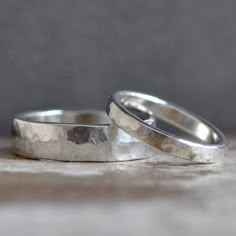 two silver wedding rings sitting on top of a wooden table next to each other,