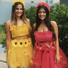 two young women standing next to each other in front of some bushes and flowers on their heads