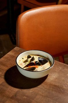 a bowl of soup with mussels in it sitting on a wooden table next to a brown chair