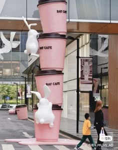 two people walking past a tall pink cup sculpture