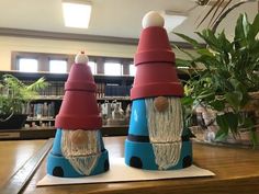 two blue and red gnomes sitting on top of a wooden table next to a potted plant