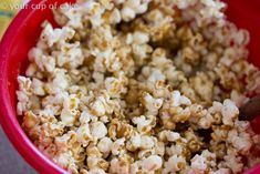 a red bowl filled with popcorn on top of a table next to a wooden spoon